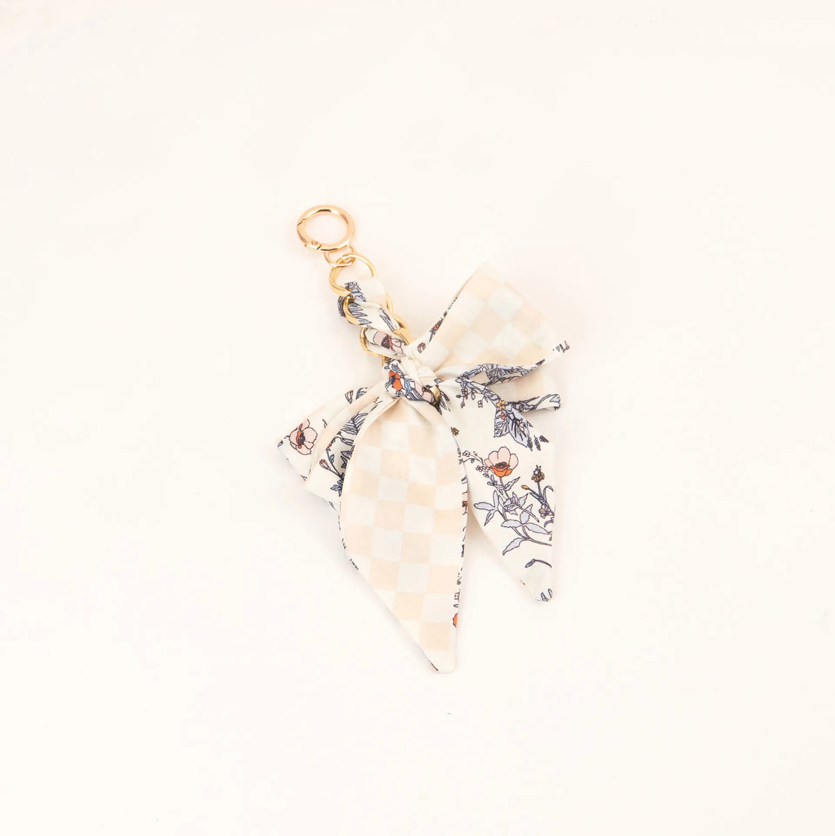 Lazo de cinta de seda floral beige y negro atado en un nudo con anillo de llavero dorado.