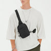 Modelo masculino vistiendo camiseta blanca y pantalones oliva, sosteniendo una bolsa cruz multifuncional negra.