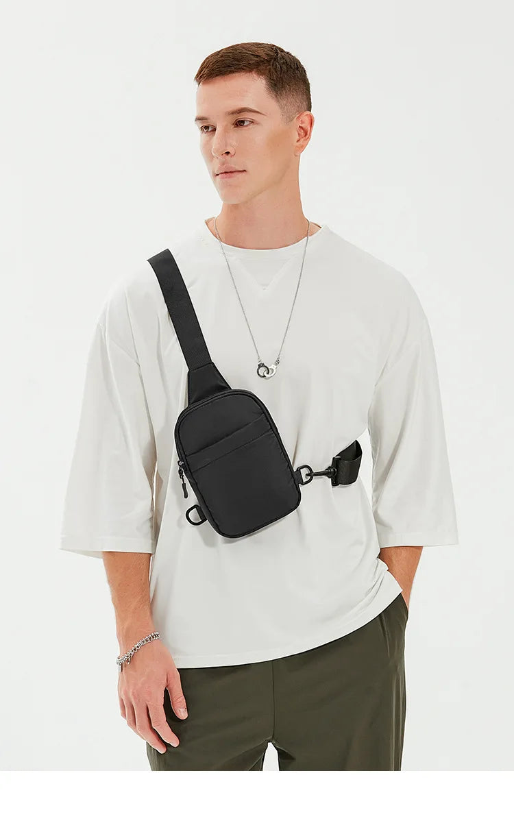 Modelo masculino vistiendo camiseta blanca y pantalones oliva, sosteniendo una bolsa cruz multifuncional negra.