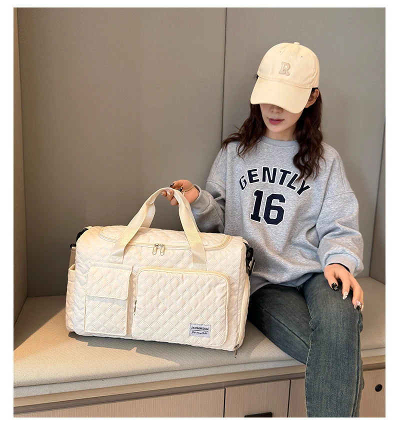 Eine Frau trägt eine beige Baseballkappe und ein graues Sweatshirt und hält eine weiße gesteppte Umhängetasche.