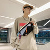 A young man wearing a beige sweatshirt and a brown hat holds an orange and black nylon chest rig bag.