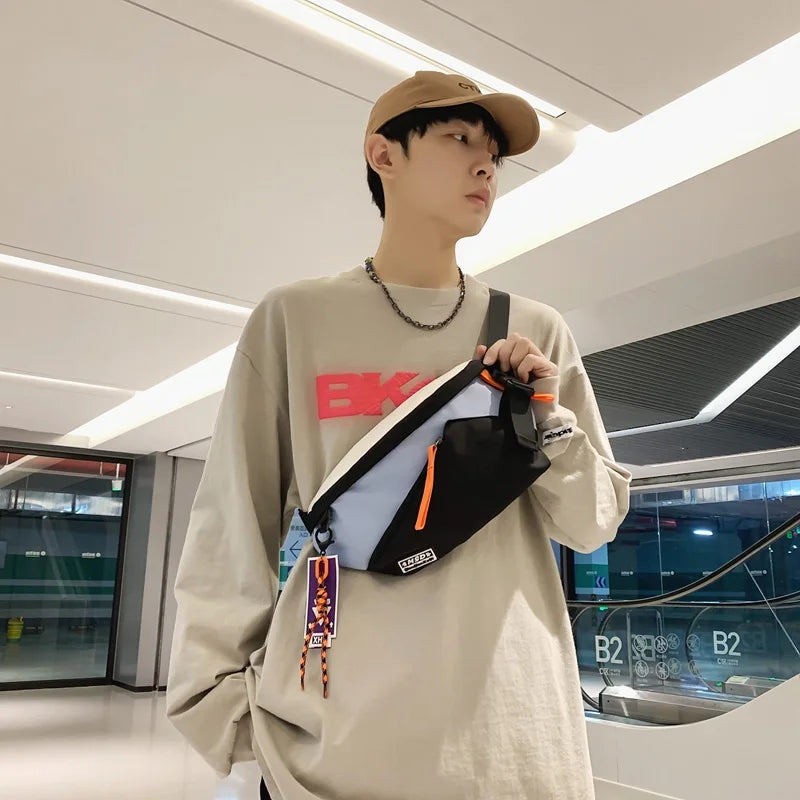 A young man wearing a beige sweatshirt and a brown hat holds an orange and black nylon chest rig bag.