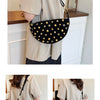 A woman models a black faux suede hobo crossbody bag with gold rivet accents against a light background.