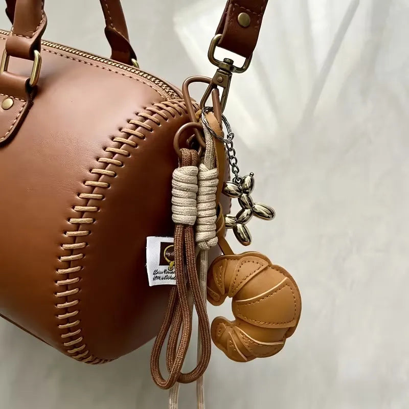 A brown leather bag with a quilted texture and a gold-toned keychain featuring a croissant pendant.