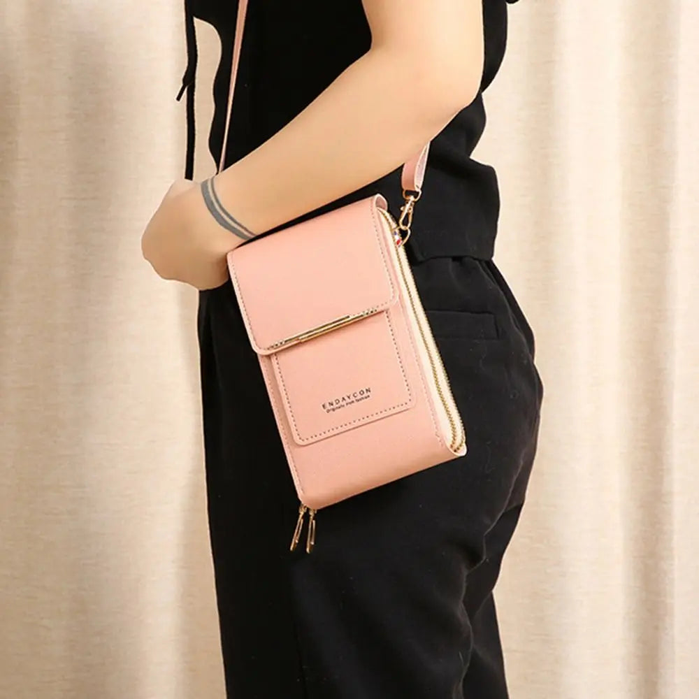 A light pink RFID-protected touch screen crossbody bag with gold hardware being held by a person.