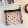 A clear mesh cosmetic storage pouch with small black hearts is displayed on a white surface.