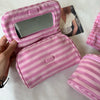 A pink striped makeup bag with a flip-top mirror is being held, showing the interior and exterior of the product.