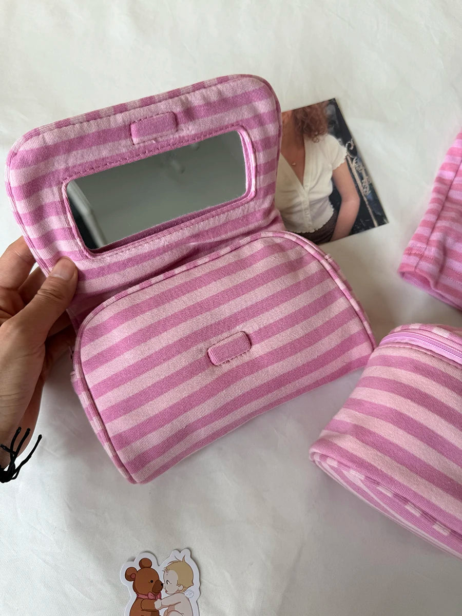 A pink striped makeup bag with a flip-top mirror is being held, showing the interior and exterior of the product.