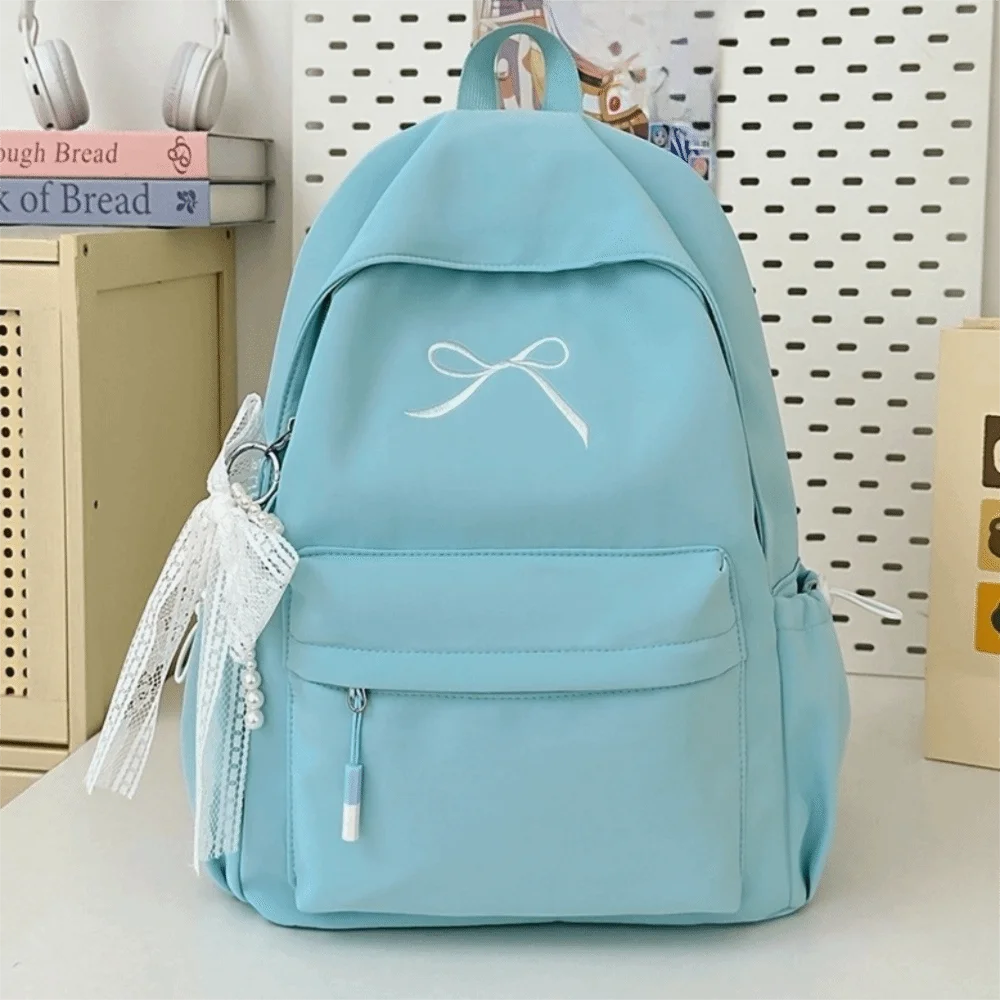 A light blue embroidered backpack with a white bow and decorative lace is shown against a white background.