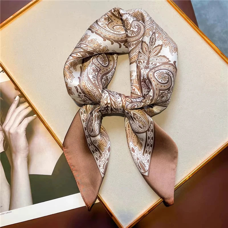 A rolled elegant paisley silk hair scarf and headband displayed on a light wooden surface.