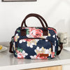 A navy blue thermal storage bag with a floral pattern and brown handles resting on a white surface.