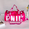 A bright pink and white printed shoulder bag with black straps is displayed on a light surface.