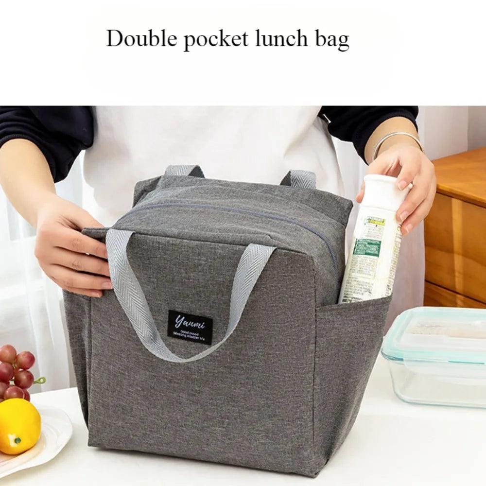 A gray insulated canvas lunch bag with double pockets is shown being held by a person.