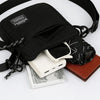 A black nylon sling bag with a leather strap is shown next to a watch and a brown card.