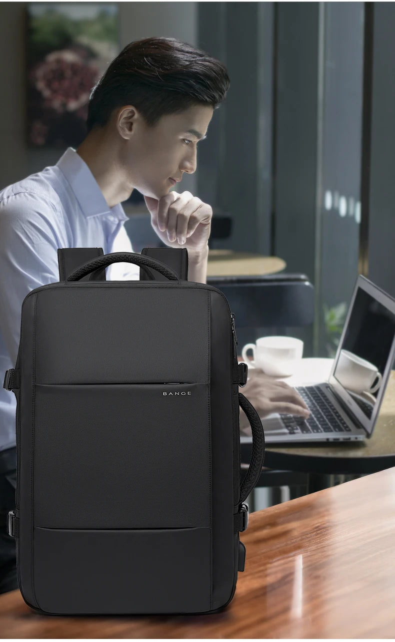A dark gray men's business travel backpack resting on a wooden table next to a laptop.