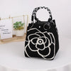 A black knitted bucket bag with a white geometric floral pattern and black and white striped handles sits next to a small pot