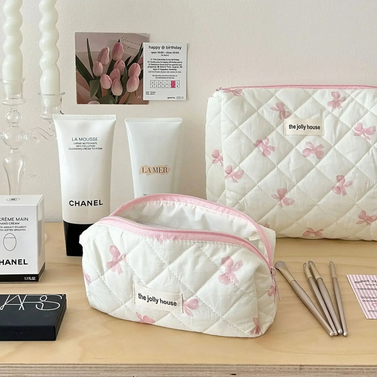Sac de rangement cosmétique blanc en quilt avec des imprimés de nœud rose sur une surface en bois avec des produits de soin e