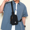 A person wearing a light blue shirt is holding a black nylon sling crossbody bag with an orange strap.
