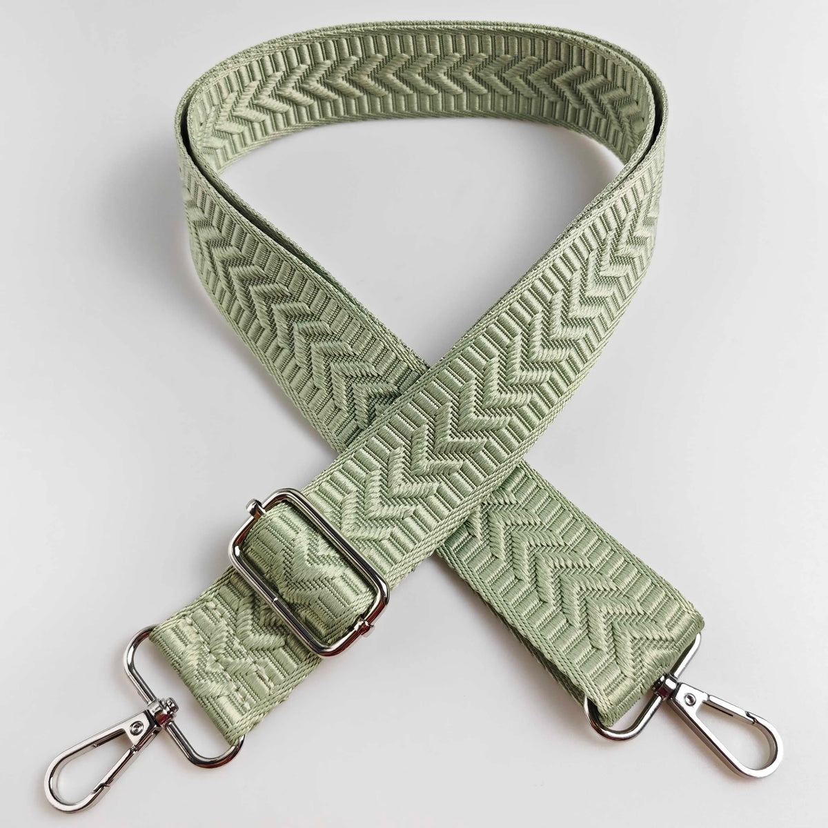 A beige woven strap with an arrow jacquard pattern, folded in an X shape.