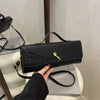 A black crocodile-embossed clutch bag with a gold clasp is displayed on a white surface.