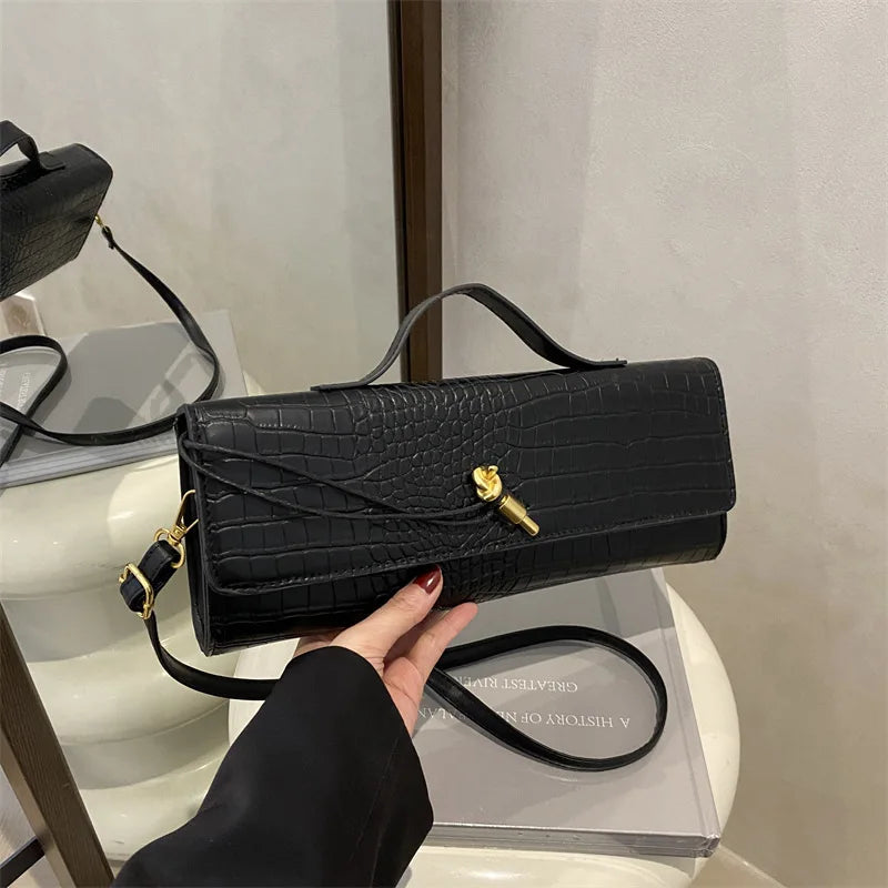 A black crocodile-embossed clutch bag with a gold clasp is displayed on a white surface.