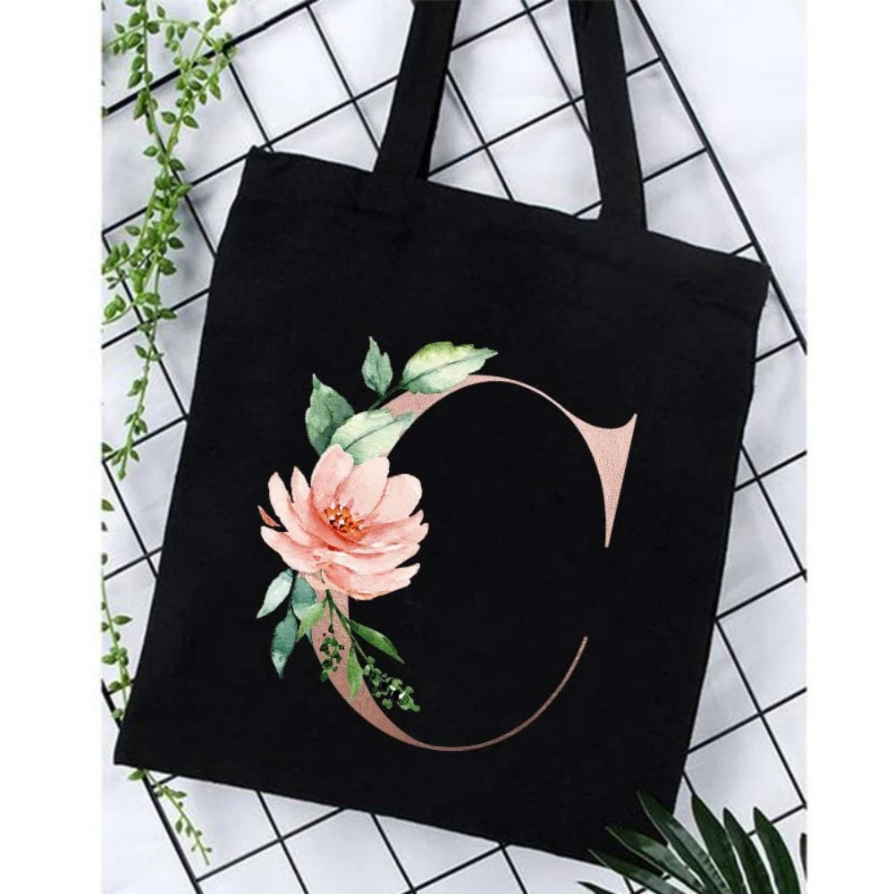 Black canvas tote bag featuring an alphabet floral print with a rose design.