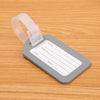 A gray luggage tag with a clear plastic strap is shown resting on a wooden surface.