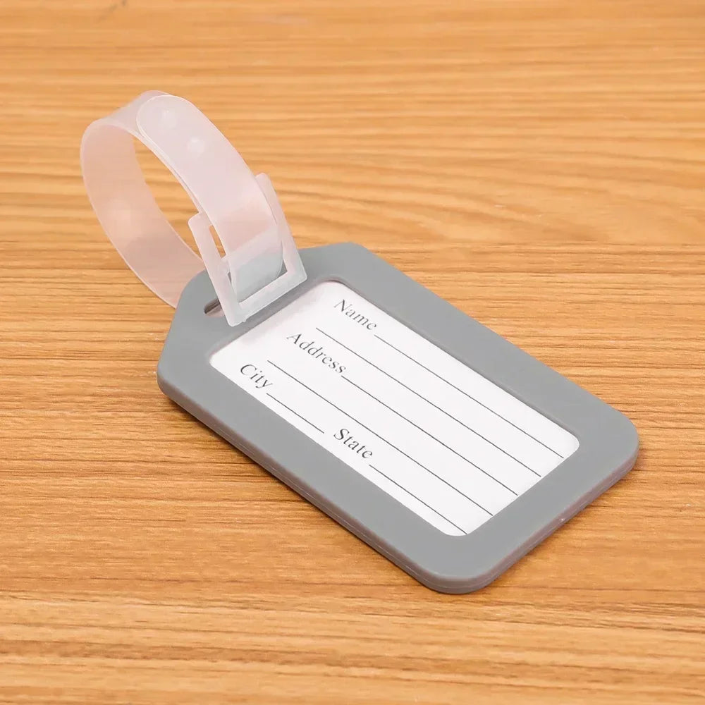 A gray luggage tag with a clear plastic strap is shown resting on a wooden surface.