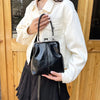 A woman holds a black leather shell handbag with a gold chain strap against a wooden background.