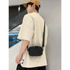 A person wearing a beige t-shirt and a brown cap is holding a black PU leather shoulder bag.