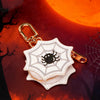 A gold-toned keychain accessory shaped like a white, spiky spider on a dark background with an orange moon.