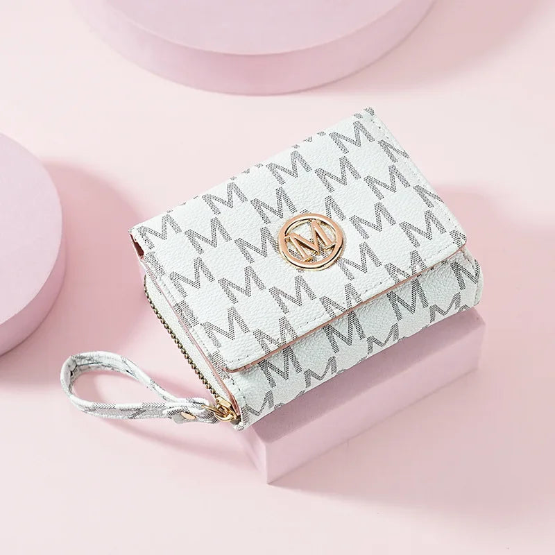 A light gray patterned letter zipper wristlet wallet resting on a pink surface.