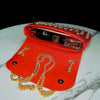 A red evening clutch bag adorned with rhinestones and featuring a diamond chain resting on a white marble surface.