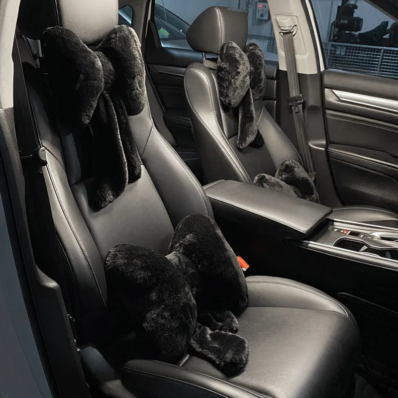 Interior view of a car seat showing black leather upholstery and fuzzy bowknot headrest pillows.