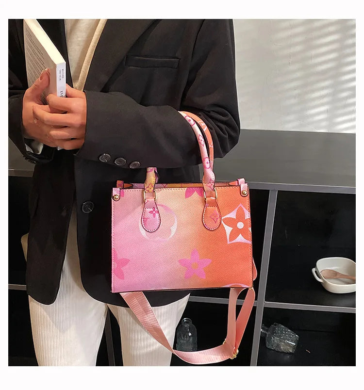A pink and orange ladies shoulder tote bag is held by a person wearing a black blazer.
