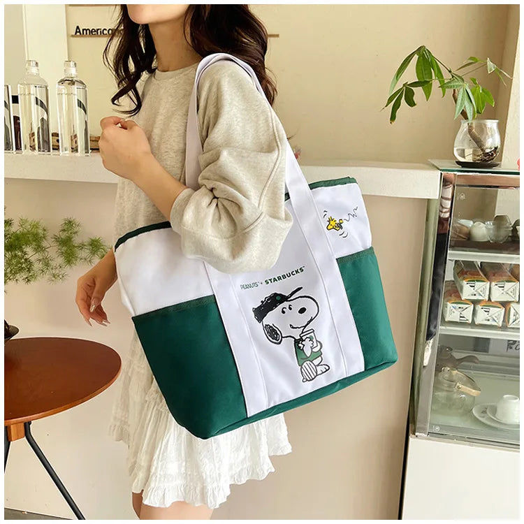 A woman holds a white and green canvas tote bag featuring a Snoopy design.