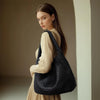 A woman models a black woven faux leather tote bag with a matching clutch against a neutral background.