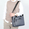 Un hombre con suéter beige y camisa blanca lleva un bolso bandolera gris horizontal.