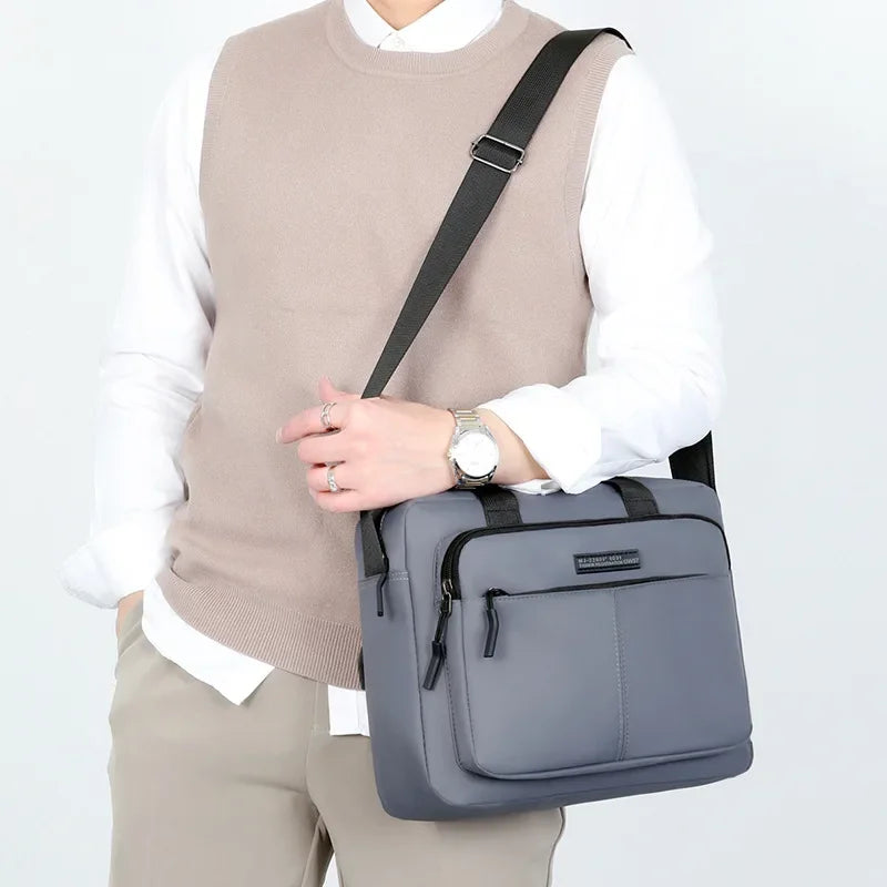 Un hombre con suéter beige y camisa blanca lleva un bolso bandolera gris horizontal.