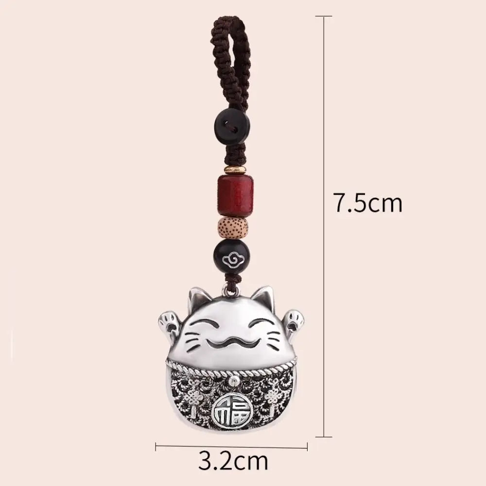 A silver lucky cat charm keychain with a dark brown beaded string and measuring lines.