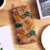 A close-up of a bohemian wood-grain leather wallet featuring floral patterns in orange, green, and brown tones on a wooden su
