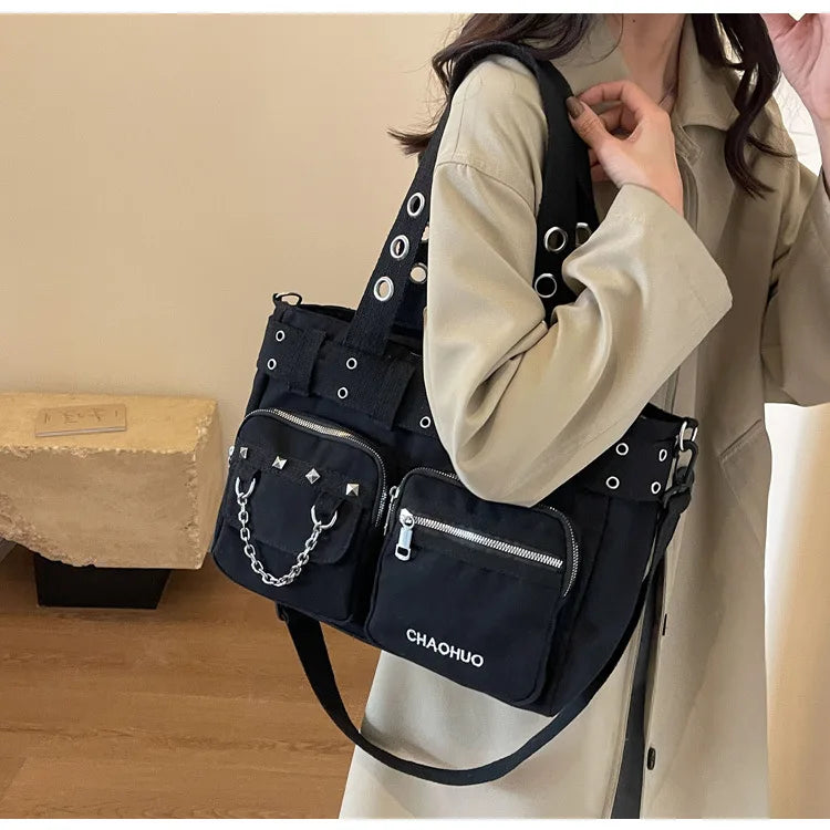 A woman is holding a black nylon shoulder bag with silver chains and rivets against a light beige coat.