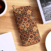 A patterned leather wallet with multiple card slots rests on a wooden surface next to a cup and a notebook.