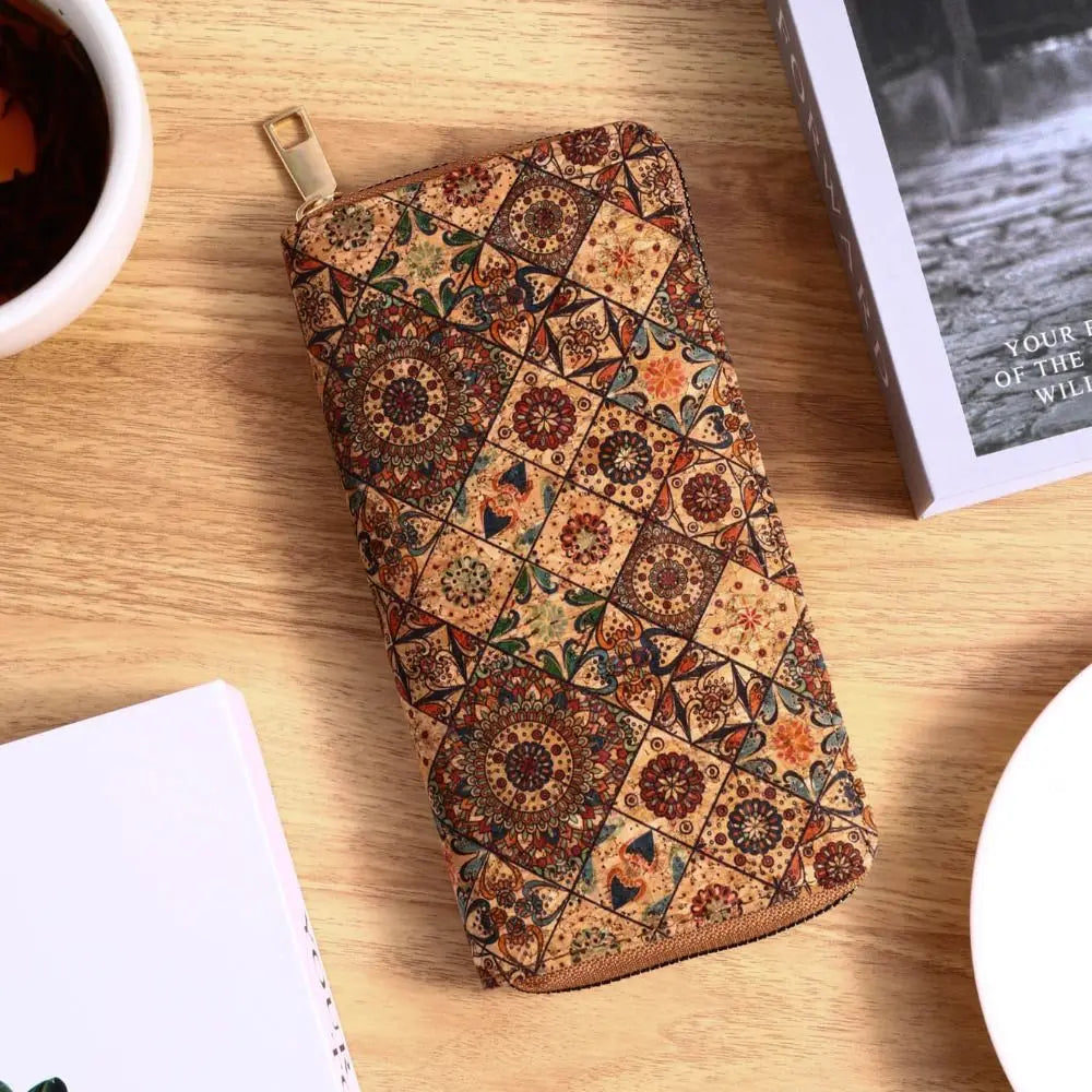 A patterned leather wallet with multiple card slots rests on a wooden surface next to a cup and a notebook.