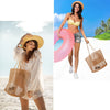 A woman wearing a white sheer dress and a woven mesh beach tote stands on the sand with a pink inflatable ring and a straw ba