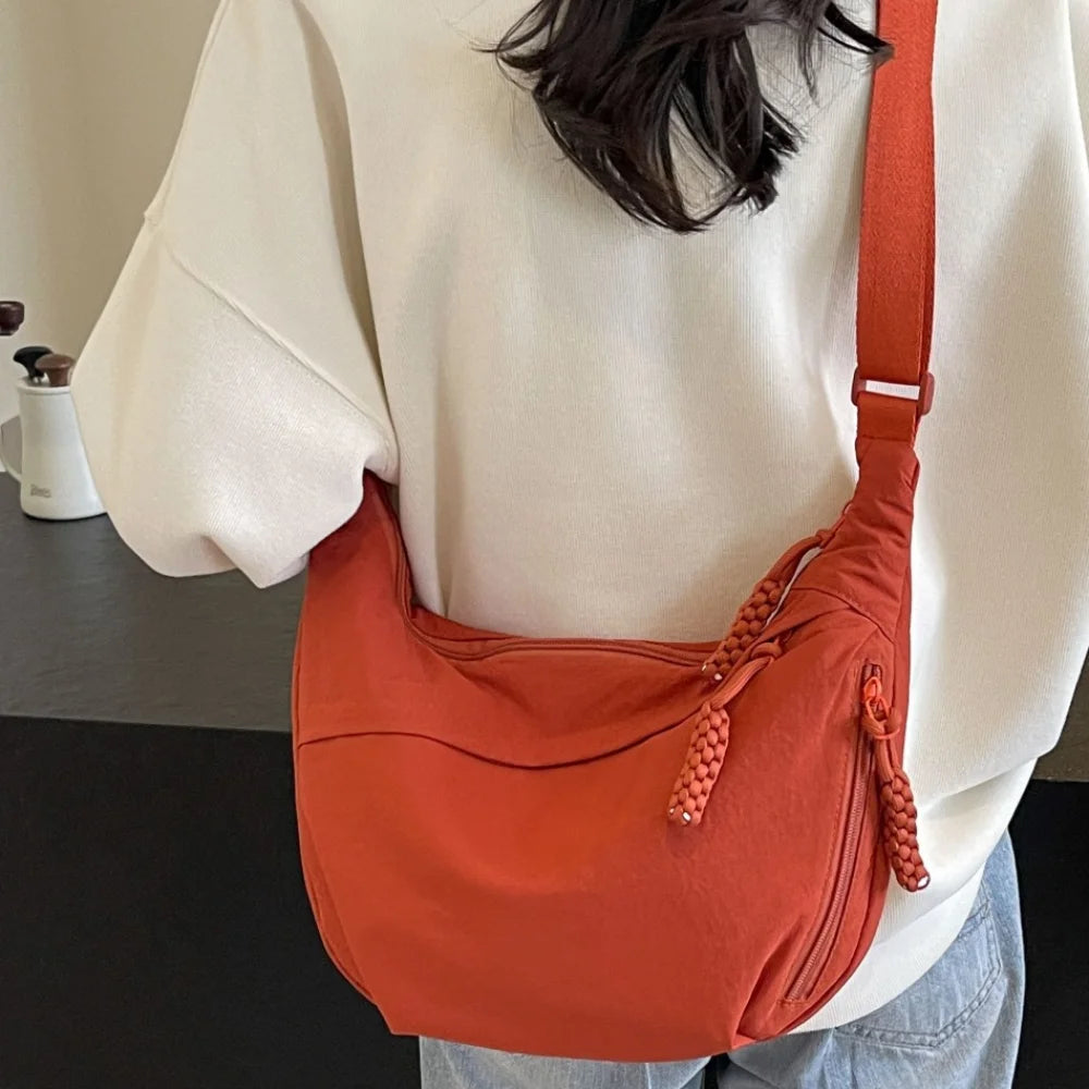 A close-up of an orange canvas crossbody shoulder bag worn by a person, set against a white top.