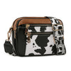 A black and white cow print PU leather crossbody bag with brown trim and gold hardware.