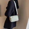 A woman is holding a light green vegan PU crossbody bag with a white striped strap against a neutral background.