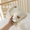 A hand is holding a cream-colored maternity and baby diaper bag tote with brown bear designs.