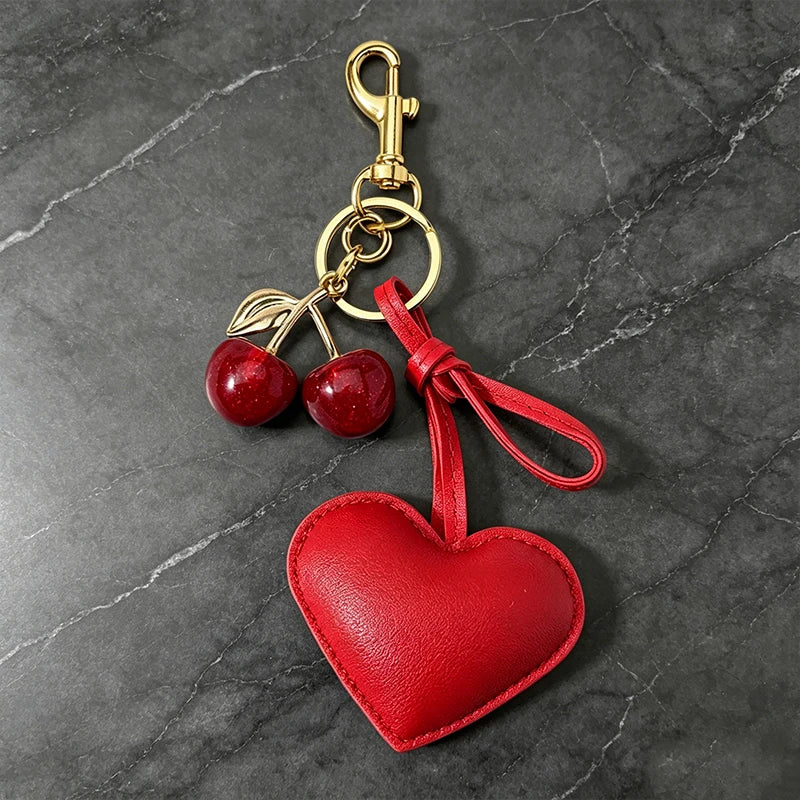 A red heart-shaped keychain featuring a cherry pendant and gold-toned hardware.